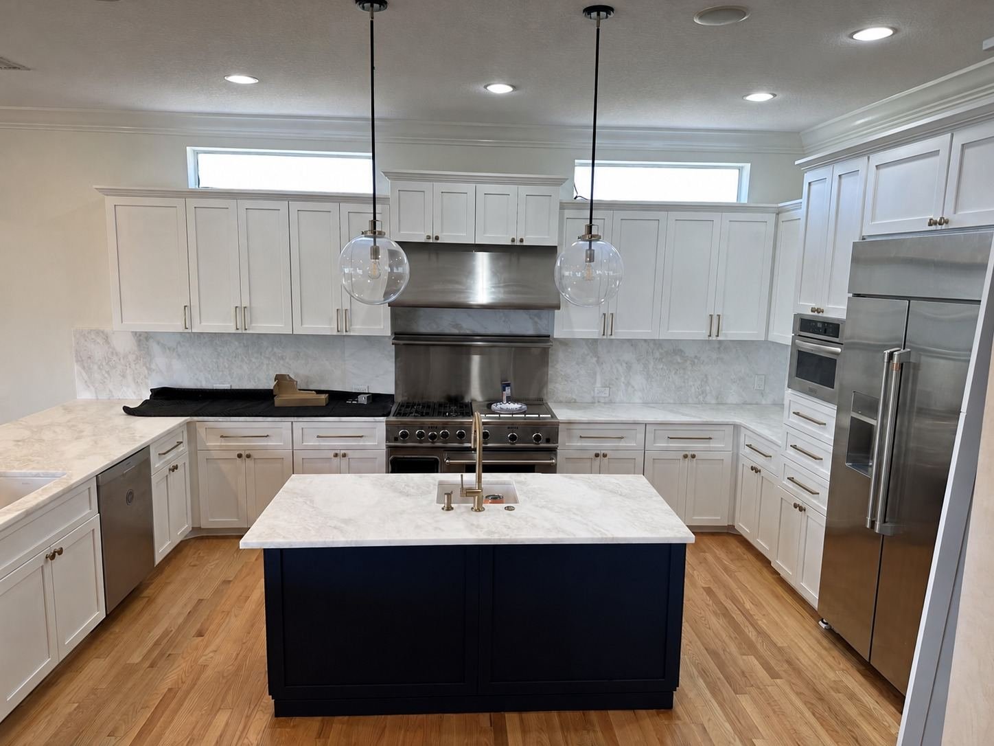 Refinished white kitchen cabinetry with a navy island and marble countertops